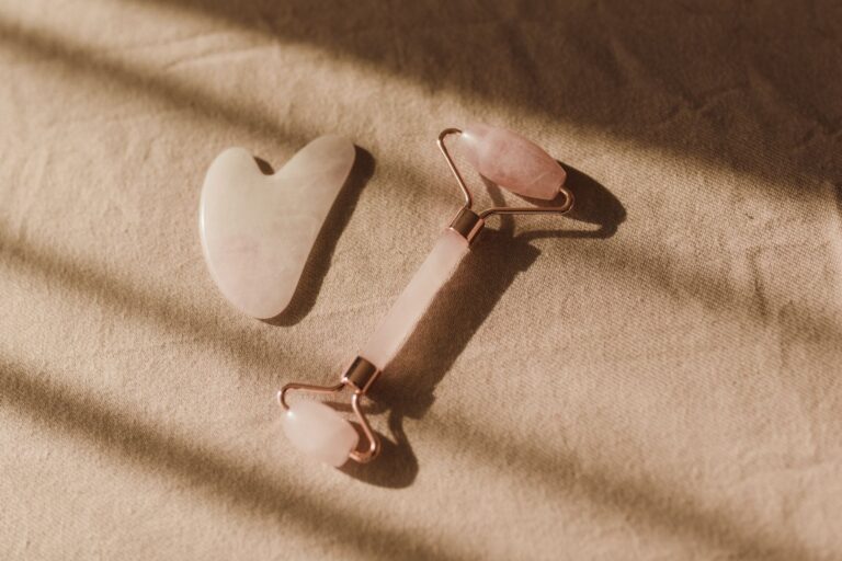 Pierre gua sha et rouleau de massage en quartz rose posés sur un tissu beige