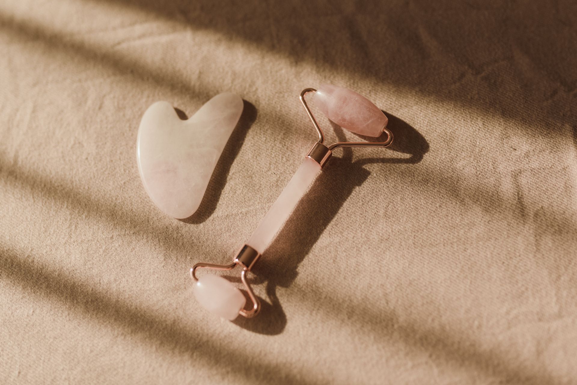 Pierre gua sha et rouleau de massage en quartz rose posés sur un tissu beige