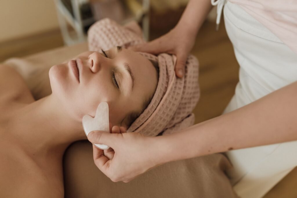 Praticienne passant une pierre gua sha sur la mâchoire d'une cliente allongée