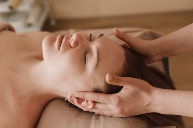 Femme allongée, les yeux fermés, pendant un massage des tempes et du visage