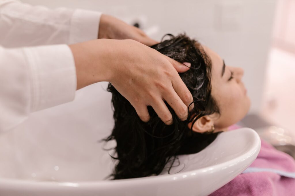 Mains massant le cuir chevelu d'une femme aux cheveux mouillés au bac à shampoing