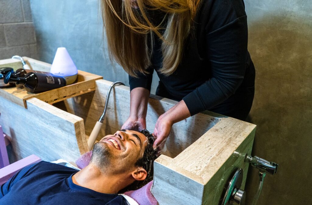 Homme souriant pendant un massage du cuir chevelu dans un bac en bois avec diffuseur d'arômes